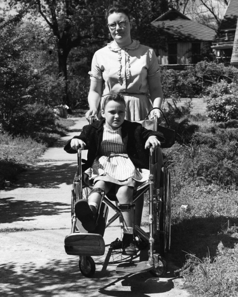Polio paralitica: bambina in carrozzina, assistita da un'infermiera